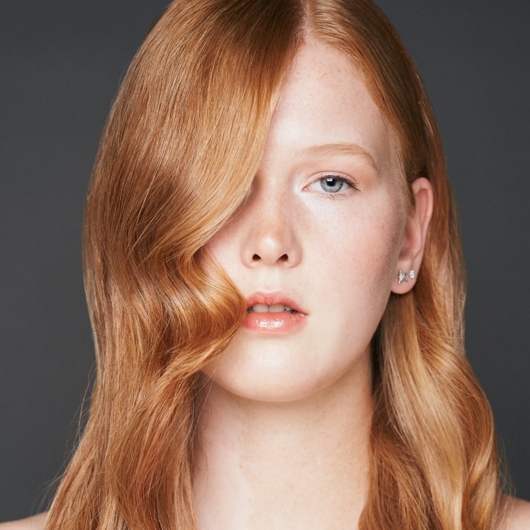 Beauty-Porträt von Miriam Rochholz: rotes, gewelltes Haar fällt über die eine Gesichtshälfte, blaue Augen, vor grauem Studiohintergrund