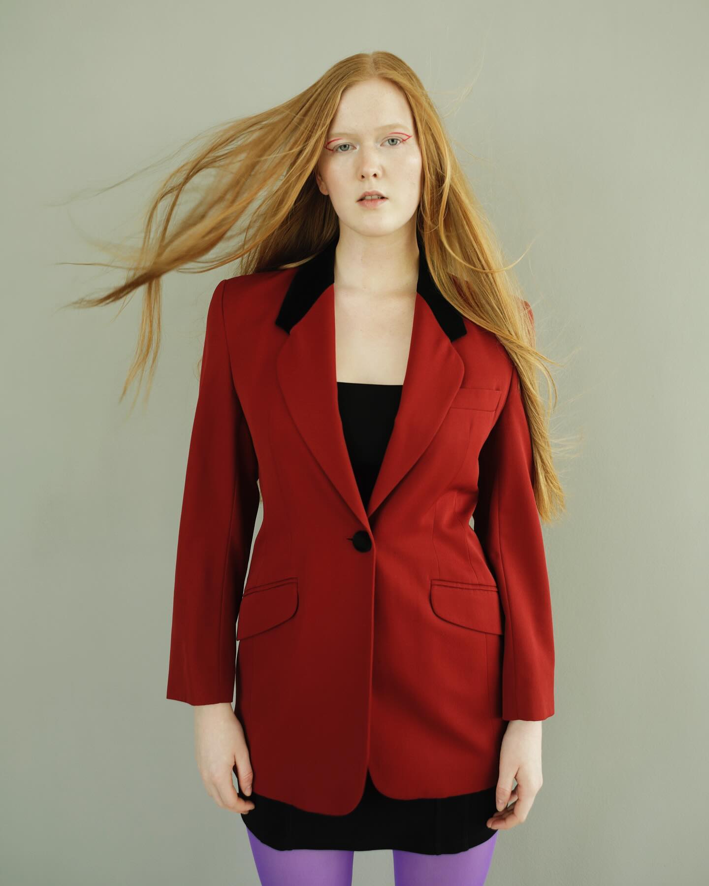 Studio-Editorial: Miriam Rochholz in rotem Blazer mit schwarzem Samtkragen, rotem Eyeliner und wehendem Haar
